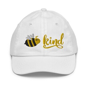 Op de afbeelding: Witte baseballpet met een geborduurde gele en zwarte bij en het woord "kind" in gele cursieve letters.