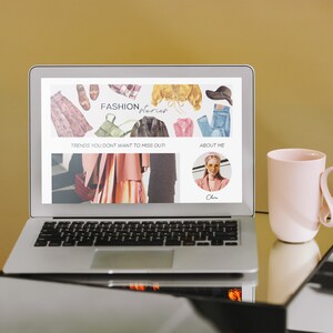 Puede incluir: Un ordenador port&aacute;til que muestra un sitio web con el texto "FASHION, Interior" y las palabras "Trends you don't want to miss out!" y "About Me". El sitio web presenta im&aacute;genes de ropa y accesorios. Una taza rosa con un asa &uacute;nica est&aacute; sobre una mesa de vidrio junto al port&aacute;til.