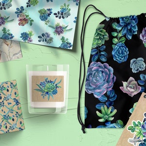 May include: A set of four different patterned papers featuring watercolor succulents in shades of blue, green, and purple. The papers are displayed on a green surface with a candle, a drawstring bag, and a notebook.