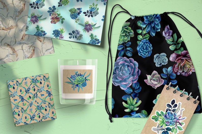 May include: A set of four different patterned papers featuring watercolor succulents in shades of blue, green, and purple. The papers are displayed on a green surface with a candle, a drawstring bag, and a notebook.