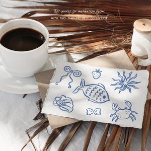 May include: A white coffee cup and saucer with dark coffee sits next to a paper with blue sea-themed illustrations. A spool of thread and dried palm leaves are also present. Text reads: "Let waves of inspiration flow with this timeless blue collection."