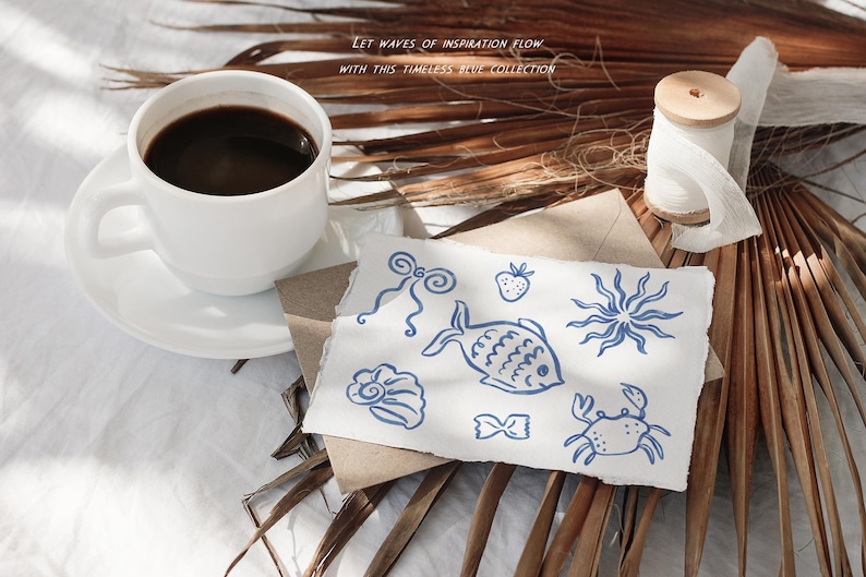May include: A white coffee cup and saucer with dark coffee sits next to a paper with blue sea-themed illustrations. A spool of thread and dried palm leaves are also present. Text reads: "Let waves of inspiration flow with this timeless blue collection."