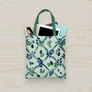 May include: A green tote bag with a white background and a blue and green floral pattern. The bag is filled with a tablet, a notebook, and a pair of glasses.