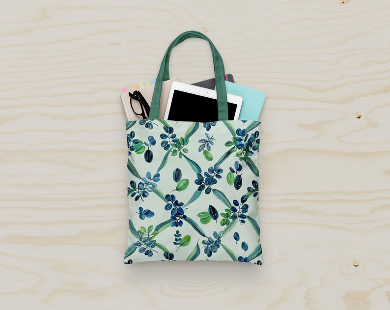 May include: A green tote bag with a white background and a blue and green floral pattern. The bag is filled with a tablet, a notebook, and a pair of glasses.