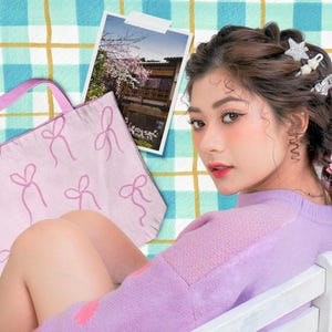 以下が含まれることがあります： ピンク色のリボンのトートバッグ、桜の咲く建物の写真、ラベンダー色のセーターを着てヘアクリップをつけた人物。背景は青と黄色のチェック柄です。