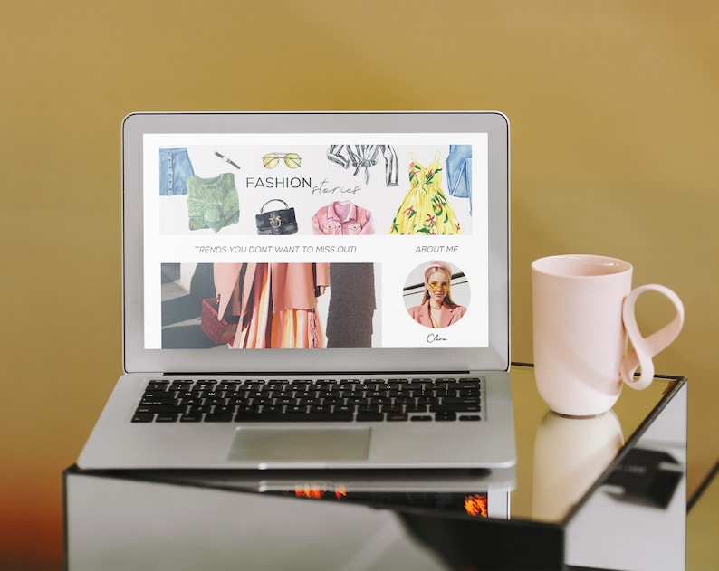 Pode incluir: Um computador port&aacute;til exibindo um site com o texto "FASHION, Stories" e imagens de roupas. O site tamb&eacute;m tem o texto "Trends you don't want to miss out!" e "About Me". Uma caneca rosa com al&ccedil;a de la&ccedil;o est&aacute; em uma mesa de vidro ao lado do laptop.