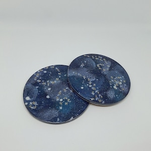 Peut inclure: Deux dessous de verre ronds avec un motif bleu foncé sur le thème de la galaxie. Les dessous de verre présentent des accents blancs et dorés en forme d'étoiles, créant un motif céleste. Les dessous de verre sont en matériau brillant.