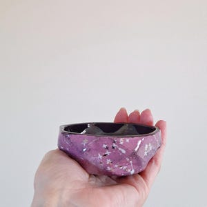 Peut inclure: Petit bol en céramique fait à la main, de forme facettée. Le bol est d'un violet vif avec des accents blancs et argentés en forme d'étoiles. L'intérieur est noir brillant. Une pièce unique pour servir ou décorer.