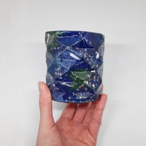 May include: A blue ceramic planter with a wavy texture and gold stars. The planter has a white and green abstract design.