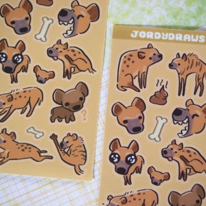 May include: A sheet of stickers featuring various cartoon hyenas in different poses. The stickers are on a yellow background with the text "JORDYDRAUS" in black at the top of the sheet.