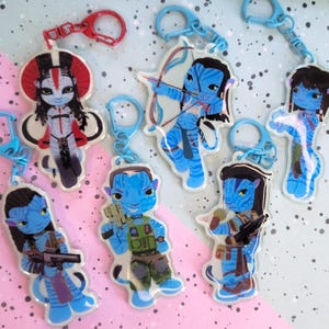 Pode incluir: Seis porta-chaves de acrílico com personagens Na'vi azuis em estilo cartoon da série de filmes Avatar. Cada personagem é retratado numa pose única com acessórios como arcos, espingardas ou equipamento tático, presos a fechos de mosquetão de plástico coloridos.