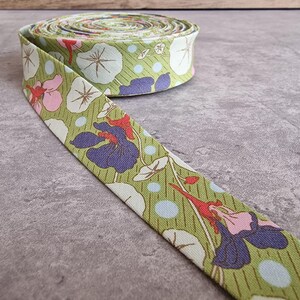Puede incluir: Rollo de cinta de tela floral con un patrón repetido de flores rosas, moradas y blancas y hojas verdes sobre un fondo verde claro. Una parte de la cinta está desenrollada.