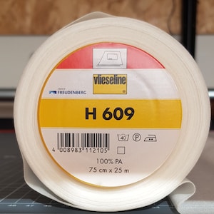 Può includere: Un rotolo bianco di tessuto di interfodera Vlieseline H 609. L'etichetta è gialla con accenti rossi e bianchi. È 100% poliammide e misura 75 cm per 25 m.