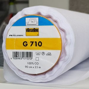 May include: A white roll of vlieseline G 710 interfacing fabric. The label is yellow with black text and a barcode. The label also includes washing instructions and the text "100% CO 90 cm x 25 m".