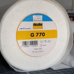 Puede incluir: Un rollo de entretela blanca Vlieseline G 770, una marca de Freudenberg, con una etiqueta amarilla que dice "100% PES, 75 cm x 25 m, crudo".