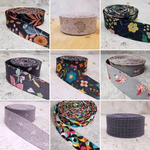 Könnte beinhalten: Eine Sammlung von neun Stoffbandrollen mit verschiedenen Mustern, darunter Blumen-, geometrische und Vogelmotive in verschiedenen Farben wie Schwarz, Grau, Blau, Gelb und Pink. Jede Rolle ist zu einer kreisförmigen Form mit flacher Kante gewickelt.