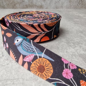 Può includere: Nastro in tessuto nero con stampa floreale e di uccelli. Il nastro presenta un uccello blu con accenti turchesi, fiori arancioni e rosa e foglie verdi su uno sfondo nero.