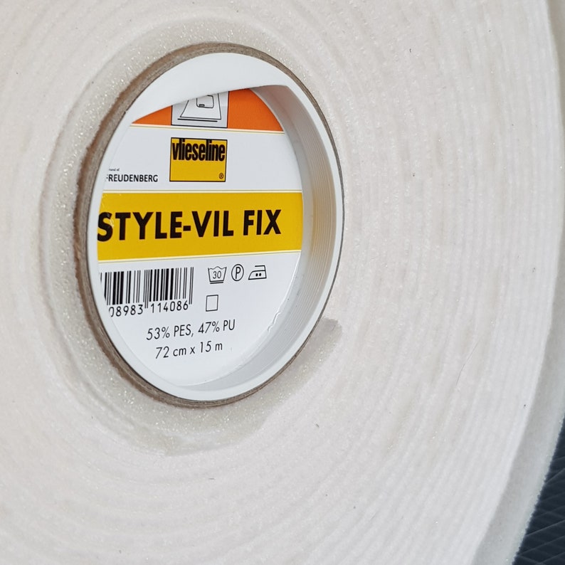 Puede incluir: Un rollo de cinta adhesiva blanca con una etiqueta amarilla que dice "vlieseline STYLE-VIL FIX". La etiqueta tambi&eacute;n incluye un c&oacute;digo de barras, instrucciones de lavado y la composici&oacute;n: 53% PES, 47% PU. La cinta mide 72 cm x 15 m.
