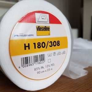 May include: A white roll of Vlieseline H 180/308 fusible interfacing with a yellow and red label. The label includes the brand name "FREUDENBERG", the product name "vlieseline", the product code "H 180/308", the barcode "4 008983 118022", and the fabric composition "85% PA, 15% PES". The label also indicates the size of the roll is 90 cm x 25 m.