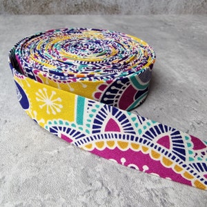 May include: A roll of colourful patterned fabric trim with yellow, pink, blue and white colours. The trim has a paisley design.