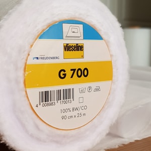 May include: A yellow and blue roll of white interfacing fabric labeled "vlieseline G 700". The label also includes the brand name "FREUDENBERG", a barcode, care instructions, and the text "100% BW/CO 90 cm x 25 m".