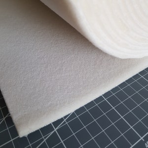Puede incluir: Primer plano de una l&aacute;mina de espuma blanca, enrollada y parcialmente desenrollada, revelando la superficie texturizada. La espuma est&aacute; sobre una estera de corte de rejilla negra.