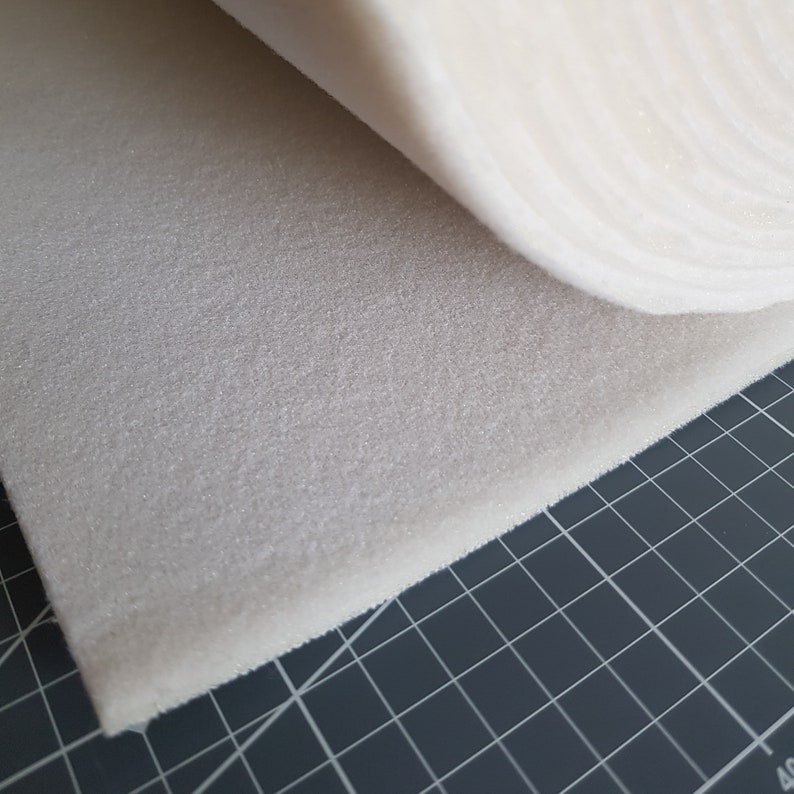 Puede incluir: Primer plano de una l&aacute;mina de espuma blanca, enrollada y parcialmente desenrollada, revelando la superficie texturizada. La espuma est&aacute; sobre una estera de corte de rejilla negra.