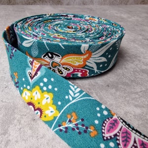May include: Teal fabric ribbon with a colorful floral pattern. The ribbon is rolled up and the pattern is visible on both the rolled up portion and the unrolled portion.