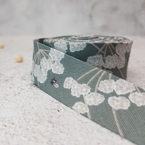 Puede incluir: Un rollo de cinta de tela verde con un patrón floral blanco. La cinta está enrollada y el patrón floral es visible en el exterior del rollo.