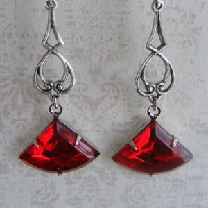 May include: A pair of silver dangle earrings with red faceted glass drops. The earrings have a delicate, ornate design.