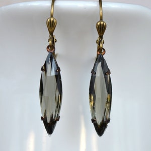 Può includere: Un paio di orecchini pendenti con un cristallo sfumato grigio sfaccettato a forma di lacrima su ogni orecchino. Gli orecchini hanno una chiusura a gancio in ottone.