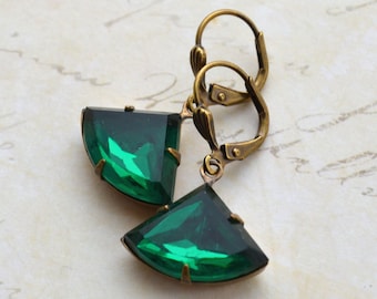 May include: A pair of emerald green gemstone earrings with antique brass hoops. The earrings feature a fan-shaped design.