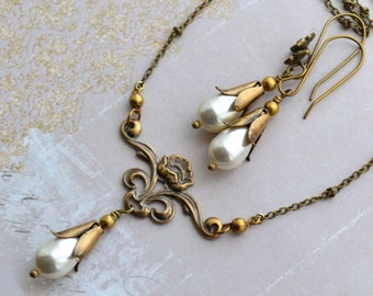 May include: Vintage gold-coloured necklace and earring set. The necklace has a floral design with a teardrop pearl pendant. Matching earrings feature pearl drops. The jewellery set is on a light background.