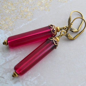 May include: A pair of earrings with long, dark pink glass tubes and antique gold-toned metal accents. The earrings have a hook closure.