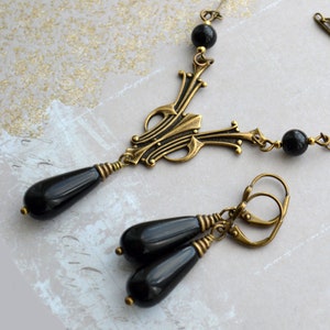 May include: A black and gold necklace and earrings set with a decorative pendant and teardrop-shaped black onyx beads.