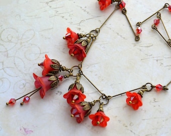 May include: A red and bronze necklace with a floral design. The necklace features multiple red glass flower charms and bronze chain links. The necklace is on a white background.