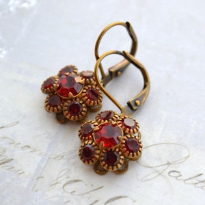 Peut inclure: Une paire de boucles d'oreilles dorées avec des accents de fleurs en cristal rouge.