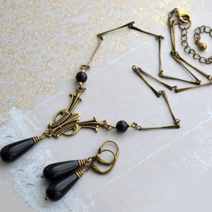 May include: A gold necklace with a black pendant and matching earrings. The pendant features a geometric design with black beads. The necklace has a chain link style.