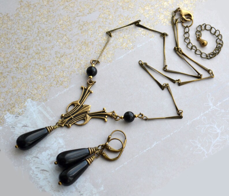 May include: A gold necklace with a black pendant and matching earrings. The pendant features a geometric design with black beads. The necklace has a chain link style.
