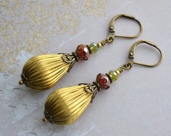 May include: Gold tone drop earrings with red and green glass beads. The earrings have a teardrop shape and are accented with ornate metal details.