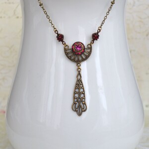 May include: A delicate gold necklace with a pink rhinestone pendant. The pendant features a crescent moon design with intricate filigree details and a dangling drop.