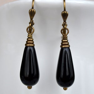 May include: A pair of black teardrop earrings with gold-toned wire wrapped accents and hooks.