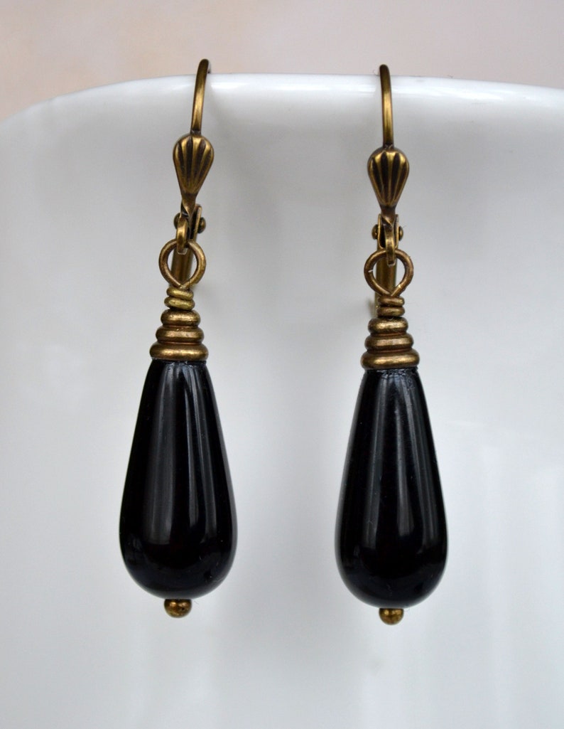 May include: A pair of black teardrop earrings with gold-toned wire wrapped accents and hooks.