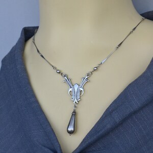 May include: A silver necklace with a detailed pendant featuring a teardrop-shaped charm. The pendant has an intricate design with a geometric pattern.