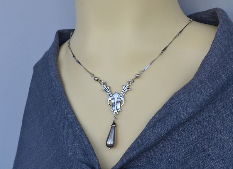 May include: A silver necklace with a detailed pendant featuring a teardrop-shaped charm. The pendant has an intricate design with a geometric pattern.