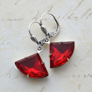 May include: A pair of silver earrings with red, faceted, triangular-shaped stones. The stones are set in a silver frame and dangle from the earrings.
