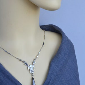 May include: A silver necklace with a teardrop pendant and an intricate design. The necklace is on a mannequin wearing a gray shirt.