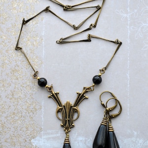 May include: A gold necklace with a black pendant and matching earrings. The pendant features a geometric design with black beads. The earrings are drop earrings with black beads.