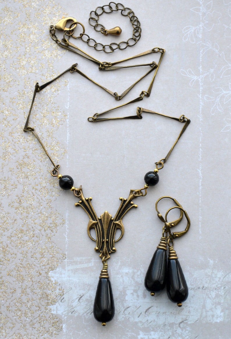 May include: A gold necklace with a black pendant and matching earrings. The pendant features a geometric design with black beads. The earrings are drop earrings with black beads.