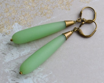 May include: A pair of dangle earrings with light green glass teardrop-shaped beads and antique brass hooks.